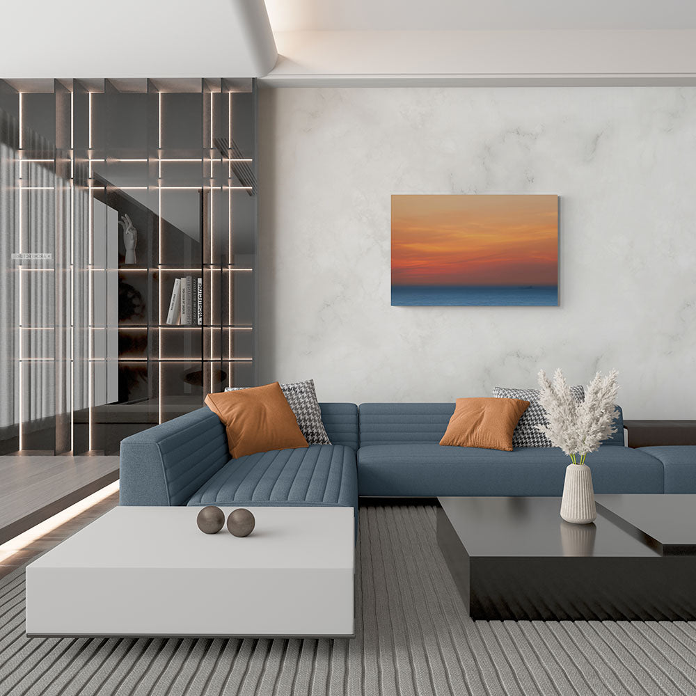 Groot canvas van een blauwe en oranje zonsondergang boven de zee, formaat 120x80cm, in een stijlvol interieur.