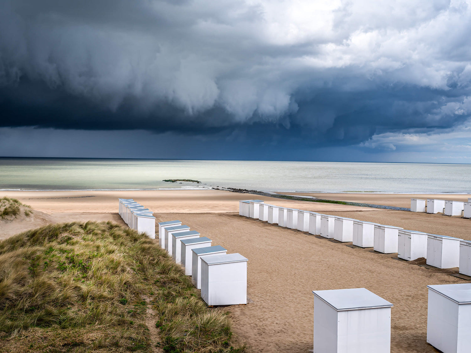 Donkere wolken boven het strand van Knokke met strandcabines en dreigende wolkbreuk aan de horizon.