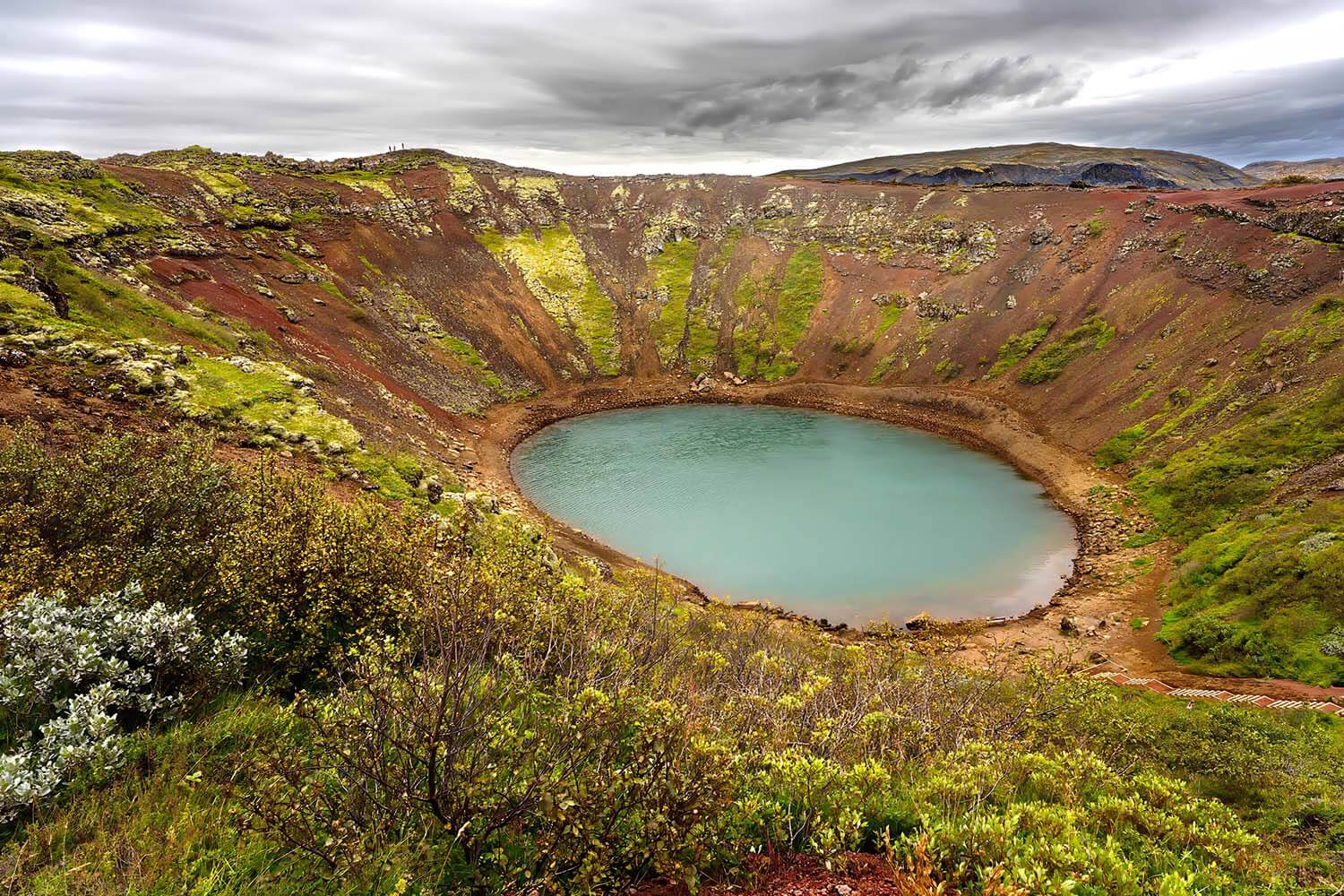 Kerið krater met turquoise water en kleurrijke rotslagen, omringd door weelderige groene begroeiing in IJsland.