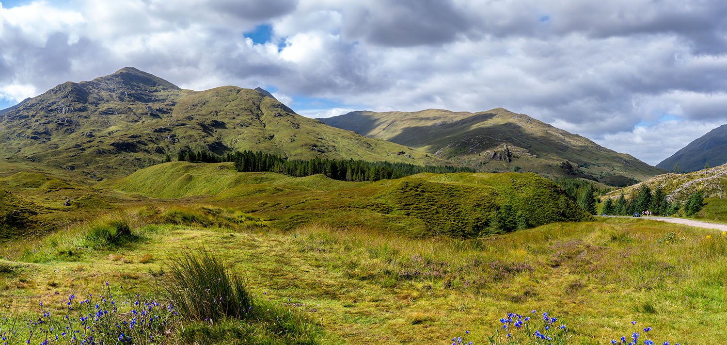 Uitgestrekte groene heuvels en bergen in de Schotse Highlands onder een bewolkte hemel.