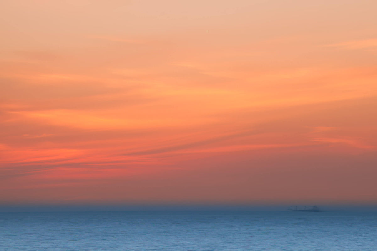 Zonsondergang met zachte blauw-oranje kleuren boven een rustige zee, met een schip in de verte.