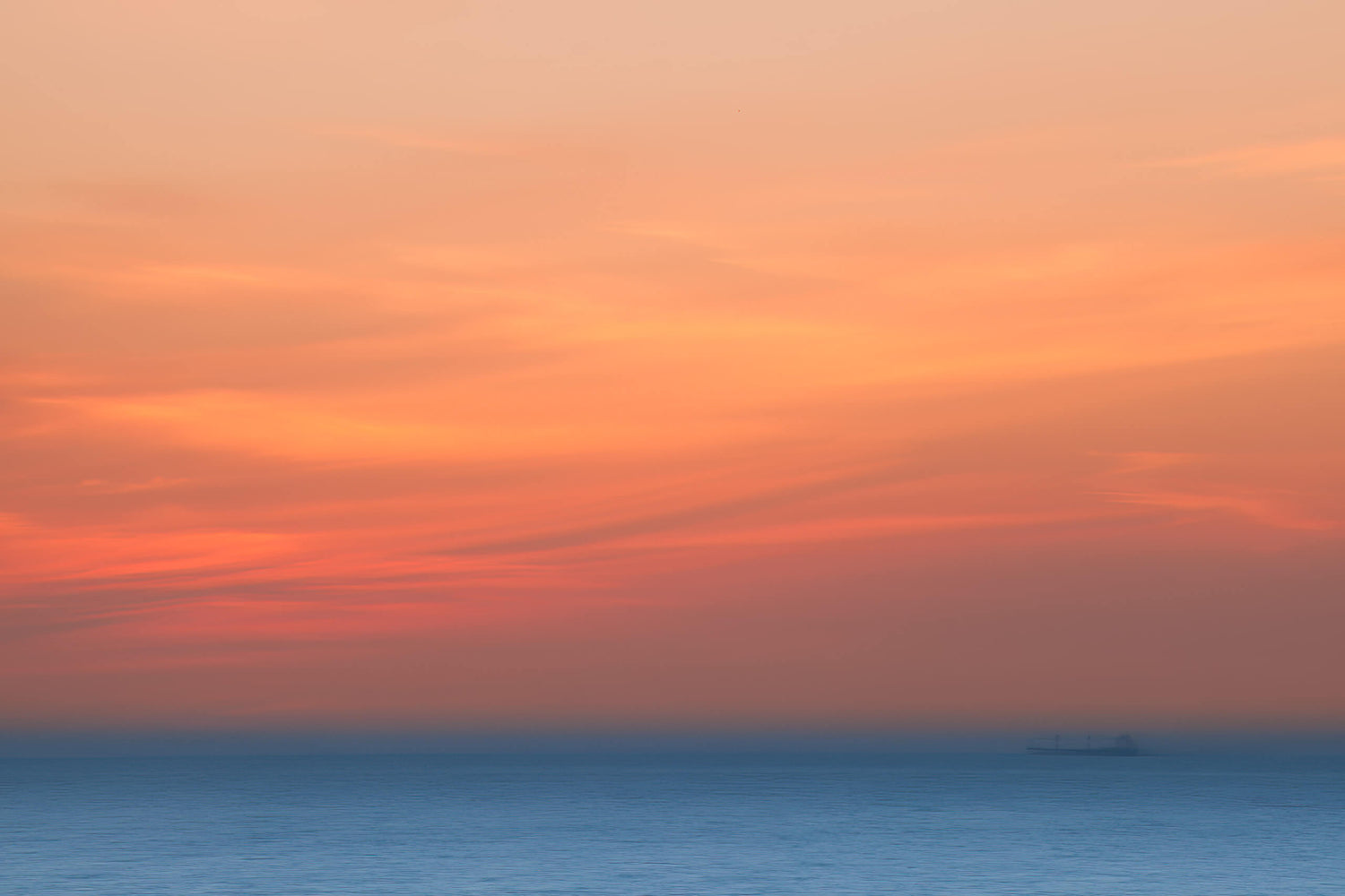 Zonsondergang met zachte blauw-oranje kleuren boven een rustige zee, met een schip in de verte.
