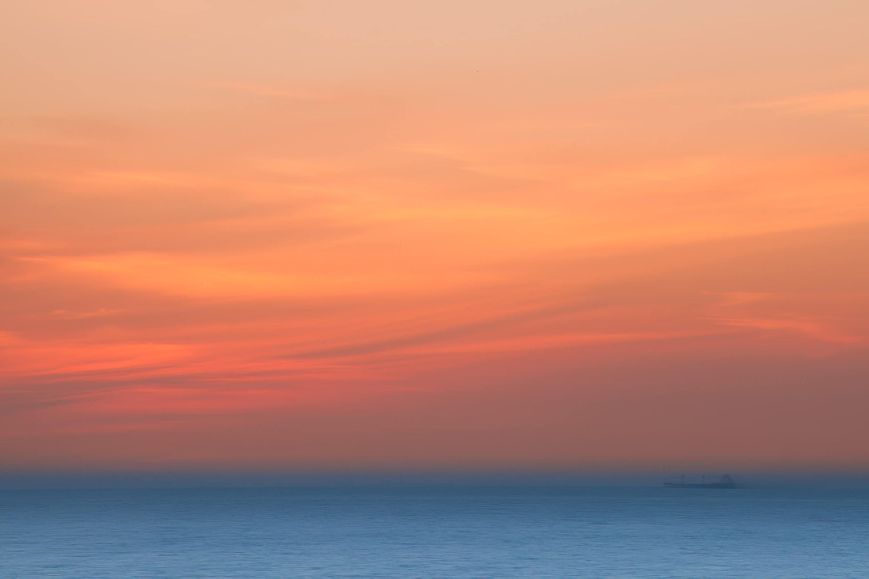 Zonsondergang met zachte blauw-oranje kleuren boven een rustige zee, met een schip in de verte.