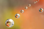 Abstracte afbeelding van zwevende waterdruppels op een warme oranje achtergrond, met reflecties van natuurlijke kleuren.