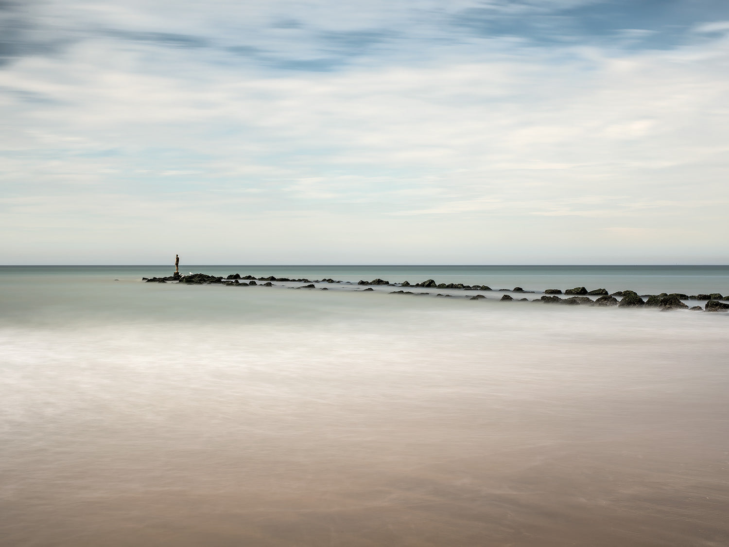 Rustig uitzicht over de zee met een golfbreker en een klein standbeeld in Knokke.