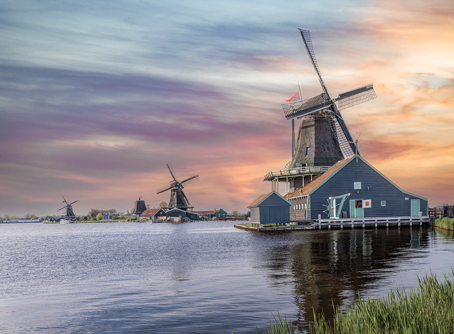 Historische windmolens aan het water in Nederland tijdens een kleurrijke zonsondergang.