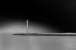 Zwart-wit foto van de moderne vuurtoren in Oostende, staande op de pier, met een dramatische, donkere lucht op de achtergrond.
