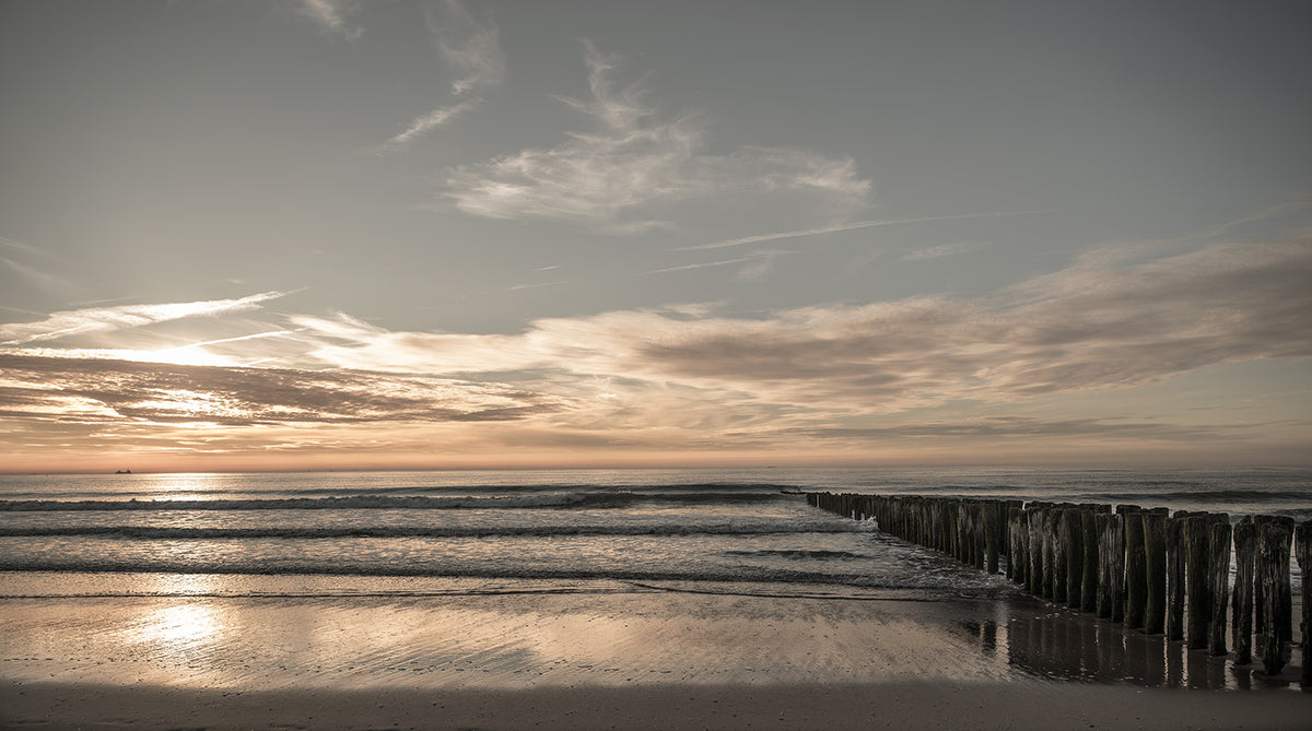 Zonsondergang aan de Noordzeekust in Knokke met een rustgevende golven en houten golfbrekers.