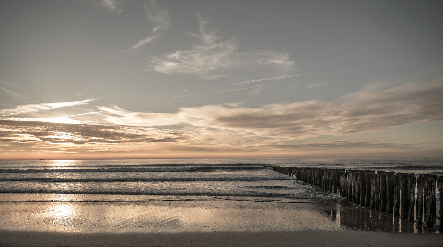 Zonsondergang aan de Noordzeekust in Knokke met een rustgevende golven en houten golfbrekers.